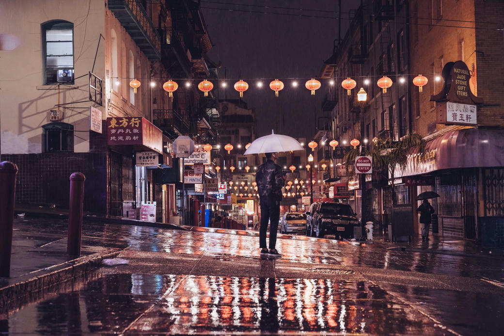 A man crosses a road in China town in the rain at night